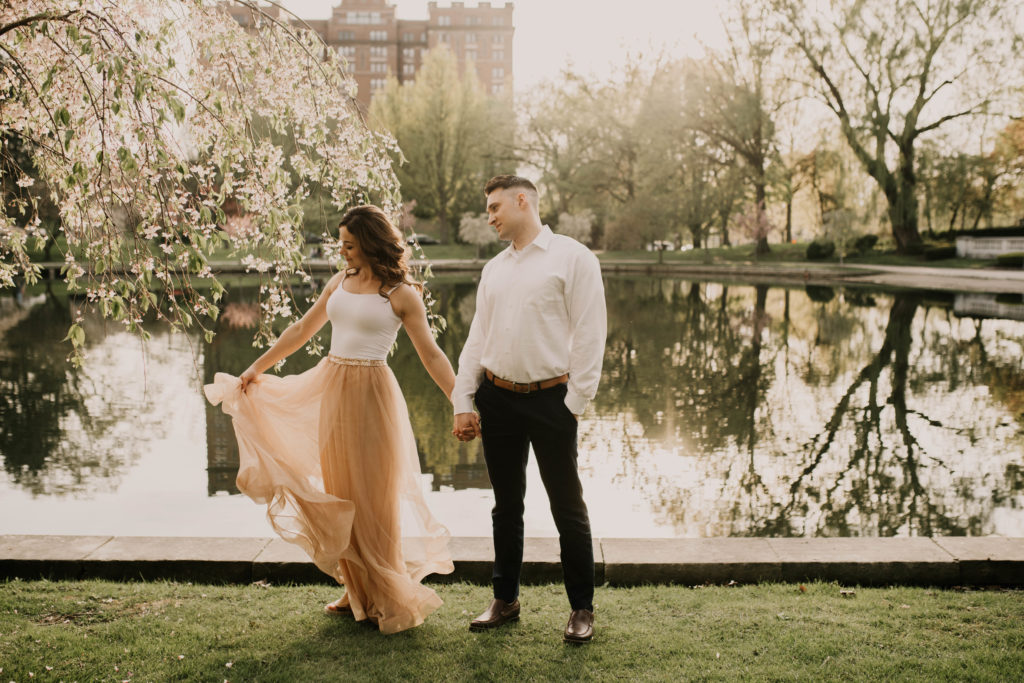 couple standing by water. woman in flowy boho pink skirt. man in button down shirt. engagement portrait photo.