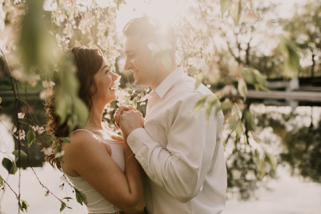Couple wearing white, romantic engagement portrait photo, leaves hanging in foreground