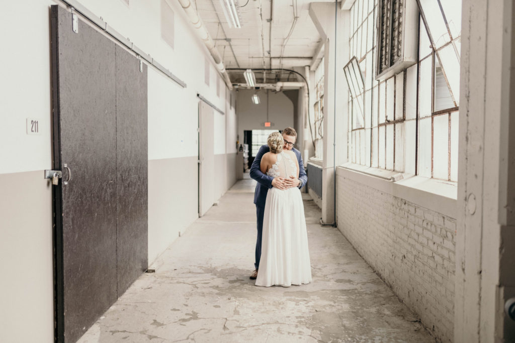 bride and groom hugging during first look in hallway on wedding day at lake erie building
