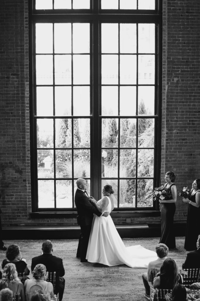 wedding ceremony at industrial wedding venue with bride and groom standing in front of large window