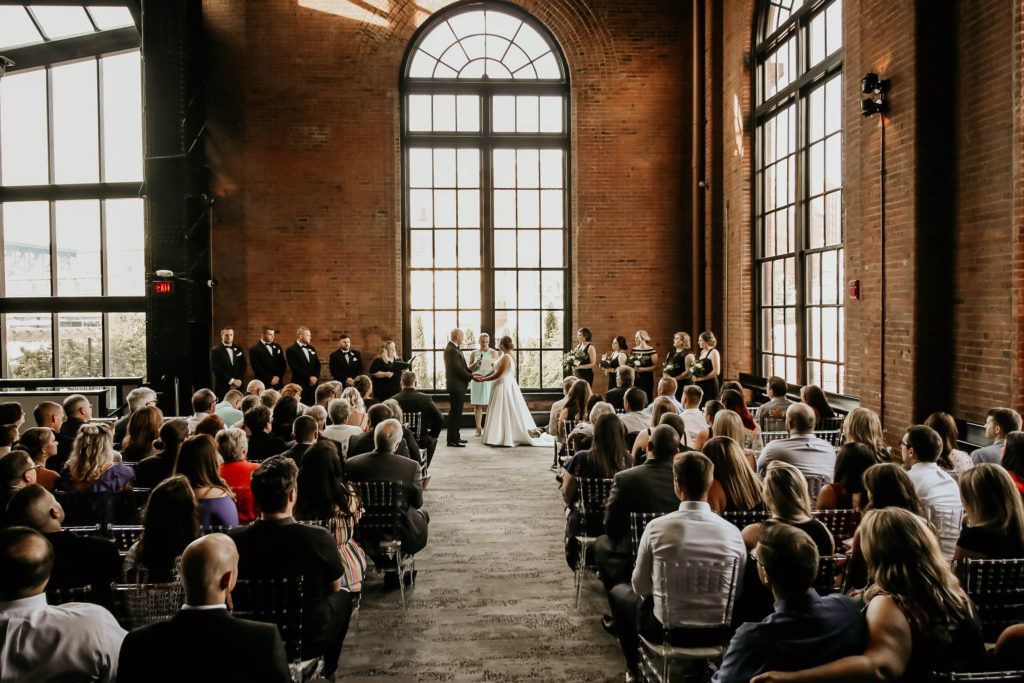 wedding ceremony at industrial wedding venue with bride and groom standing in front of large window