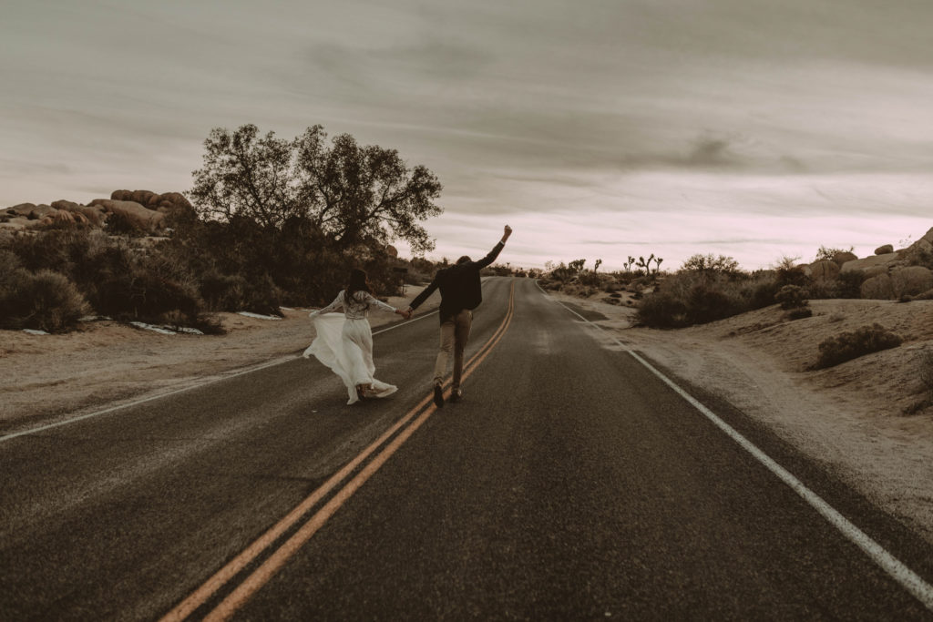 boho bride and groom holding hands running down road in joshua tree national park after eloping