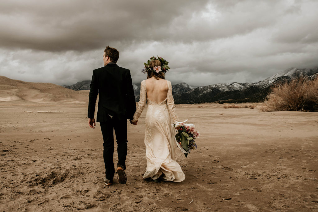 boho bride and groom holding hands in colorado sand dunes national park